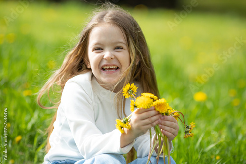 Portrait of a happy smiling little girl lying on green grass with dandelions