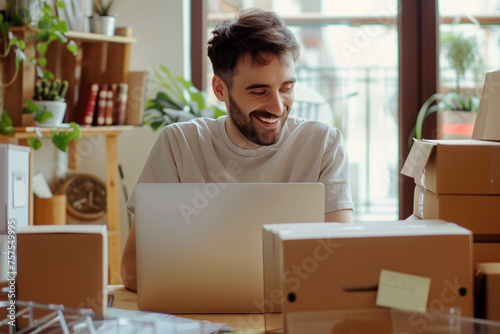 man smiling at his laptop sits at desk looking in boxes