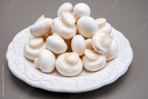 White champignon mushrooms fresh uncooked on white ceramic plate copy space
