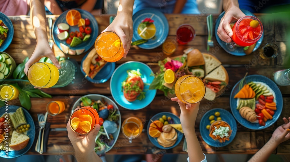 a top view on a spring brunch or picnic table with a selection of dishes and drinks and hands of family members holding glasses with beverages