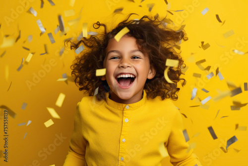A jubilant kid model celebrating a victory, against a solid wall of yellow background, throwing confetti in the air with unrestrained joy and happiness.