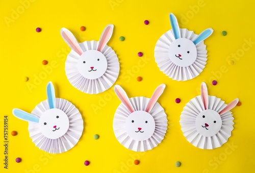 Spring, Easter holiday, on a yellow background are cute, funny Easter paper bunnies, colored candies and bright Easter eggs. Flat lay, top view. The concept of children's creativity, handmade

