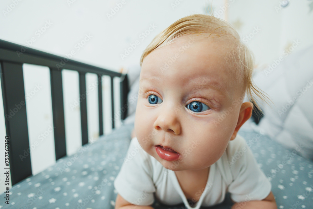 A small child is lying in a crib at home. Portrait of a five-month-old baby lying in a playpen. Cheerful happy child.