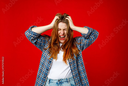 Emotional angry 30s woman screaming on red studio background. Emotional, young face. Screaming, hate, rage. Hands on the head photo