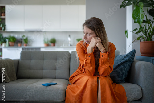 Fotografie Lonely woman anxiously stares at cellphone next to waiting for important call, message sits heartbroken from racking up unpleasant thoughts