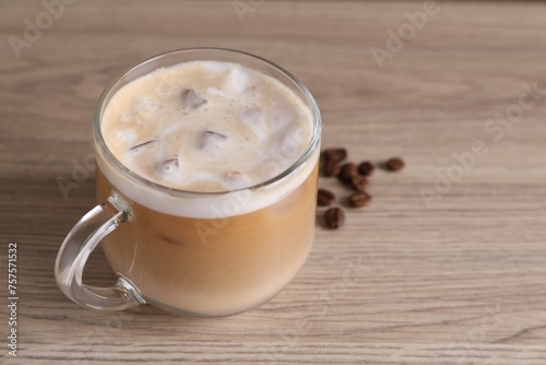 Cup of fresh iced coffee and beans on wooden table, closeup. Space for text
