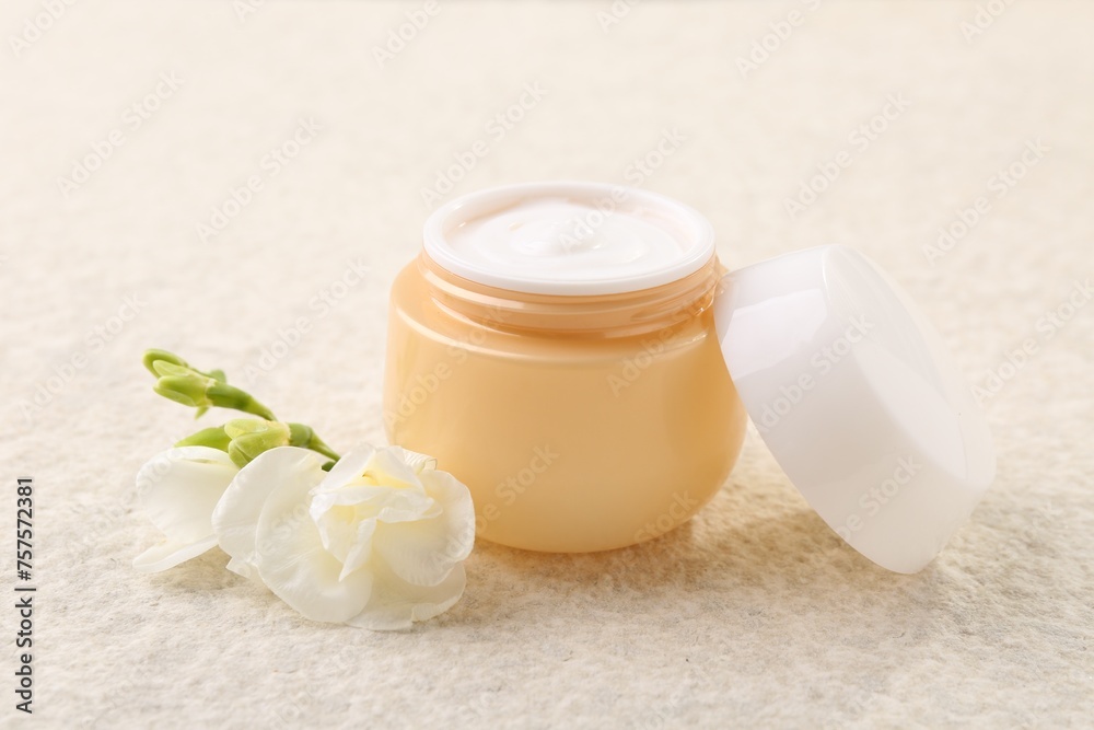Body care. Moisturizing cream in open jar and flower on light textured table, closeup Body care. Moisturizing cream in open jar and flower on light textured table, closeup