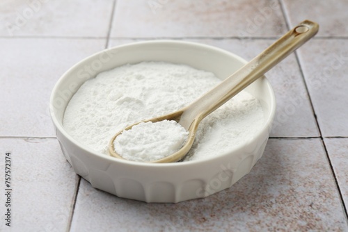 Baking powder in bowl and spoon on light tiled table, closeup
