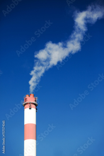 High concrete chimney. Industrial area view. Isolated on blue sky. Heating plant chimney. White smoke flowing out of the chimney. Steam in the air. Air pollution background. Production side effect.