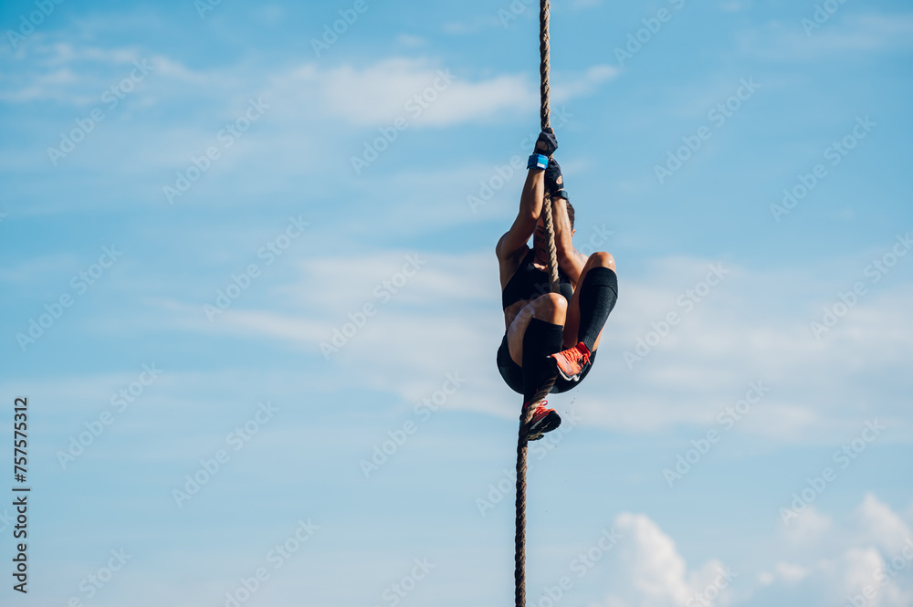 Strong woman climbing a rope while participating in an obstacle course race Strong woman climbing a rope while participating in an obstacle course race