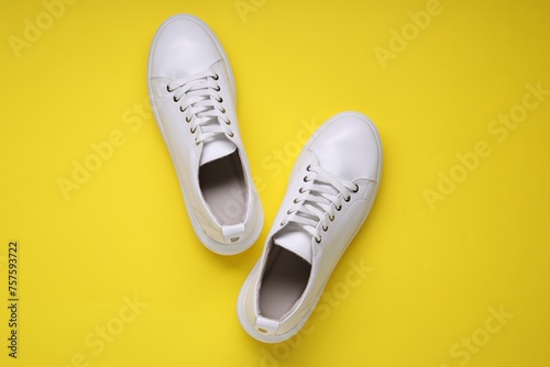 Pair of stylish white sneakers on yellow background, top view