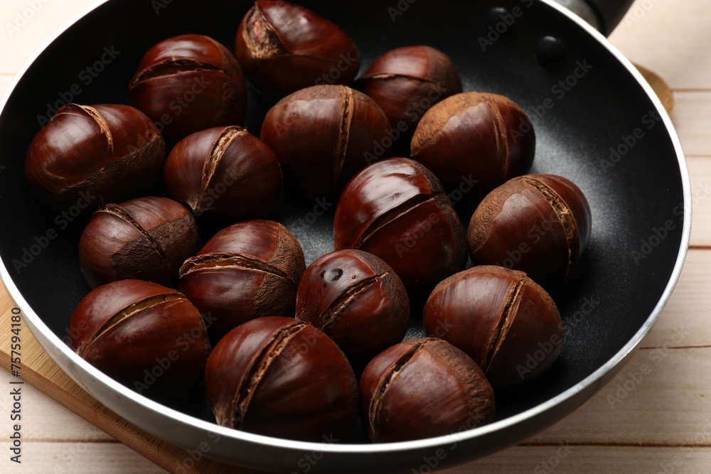 Roasted edible sweet chestnuts in frying pan on wooden table, closeup
