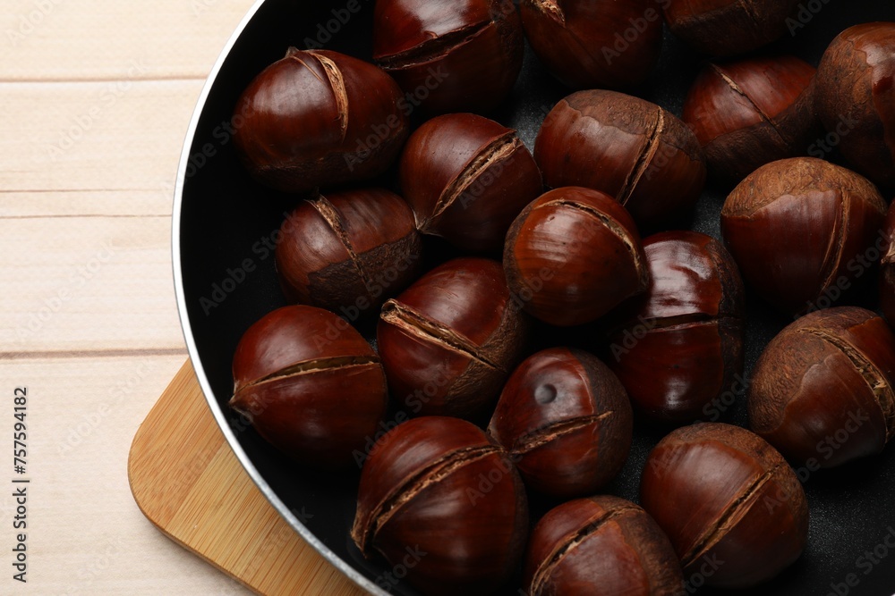 Roasted edible sweet chestnuts in frying pan on wooden table, top view Roasted edible sweet chestnuts in frying pan on wooden table, top view