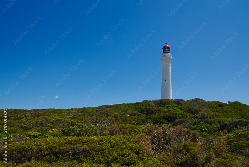 A tall white and red lighthouse stands proudly against a clear blue sky on a beautiful sunny day.
