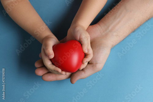 Father and his child holding red decorative heart on light blue background, top view