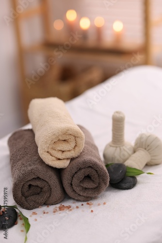 Spa stones, rolled towels and herbal bags on massage table indoors