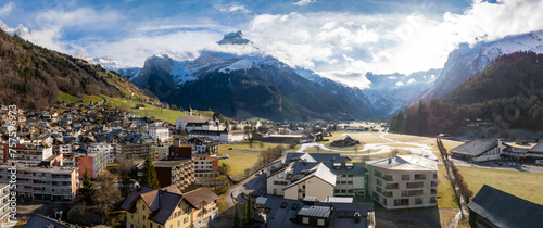 Panoramic view of Engelberg, Switzerland, showcasing its alpine village with chaletstyle buildings, a historic clock tower landmark, and snowdusted valley against a backdrop of majestic mountains. photo