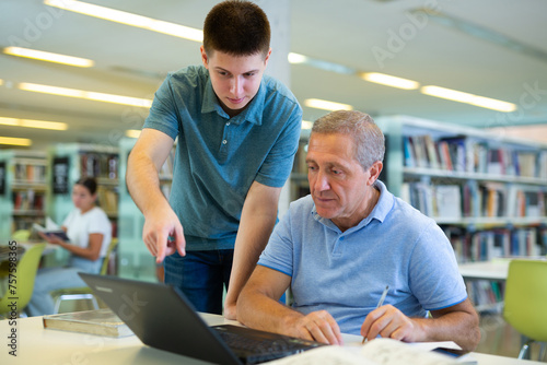Young European man tutoring a mature Caucasian male in the library