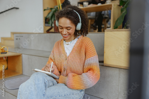 a woman wearing headphones is sitting on the floor writing in a notebook