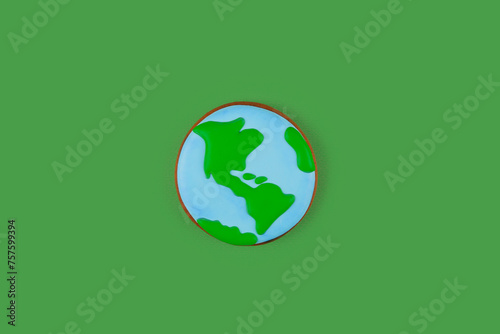 Earth Day concept. Single cookie in shape of Earth on green backdrop.