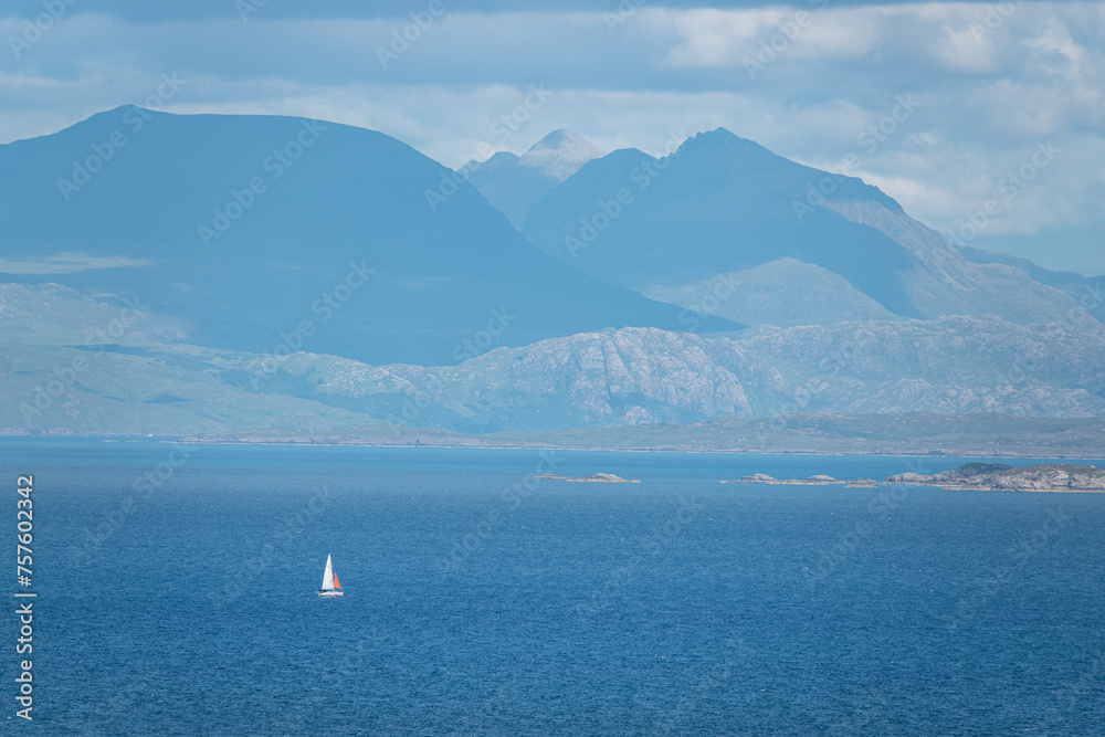 Sailboat glides on blue ocean water along scenic hilly coast of Scottish islands Sailboat glides on blue ocean water along scenic hilly coast of Scottish islands
