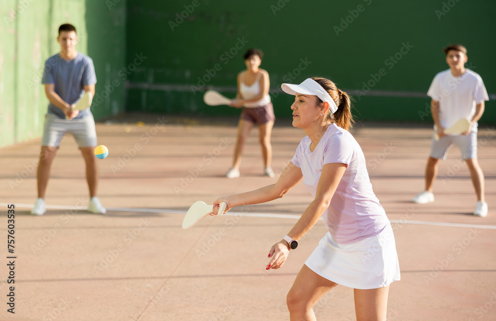 Portrait of sporty young girl playing paleta fronton on outdoor court, ready to hit ball. Healthy and active lifestyle concept