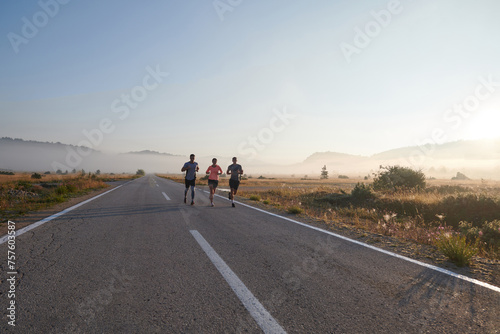 A group of friends, athletes, and joggers embrace the early morning hours as they run through the misty dawn, energized by the rising sun and surrounded by the tranquil beauty of nature
