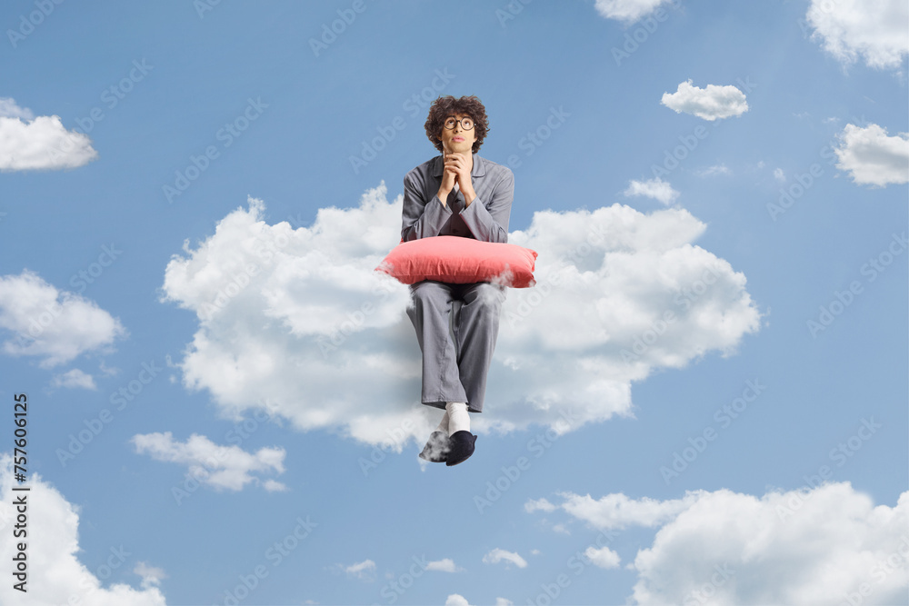 Young man in pajamas sitting on a cloud in the sky