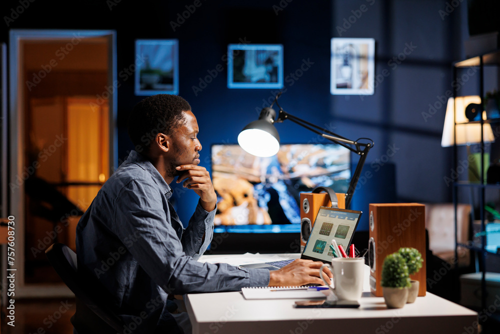 Young analyst checks financial balance and works on accounting analysis, finding ways to grow company revenue at home. African american advisor doing remote work using economy statistics. - obrazy, fototapety, plakaty 