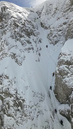 A group of mountaineers linked by a climbing rope is climbing up a snowy slope. They have helmets and safety equipment.