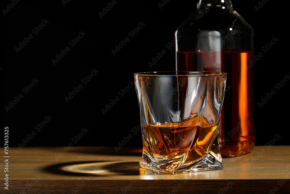 Whiskey in glass and bottle on wooden table against black background, space for text Whiskey in glass and bottle on wooden table against black background, space for text