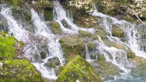 Waterfall: cascades of water falling on green stones and rocks covered with moss. Natural resource conservation and environmental protection.