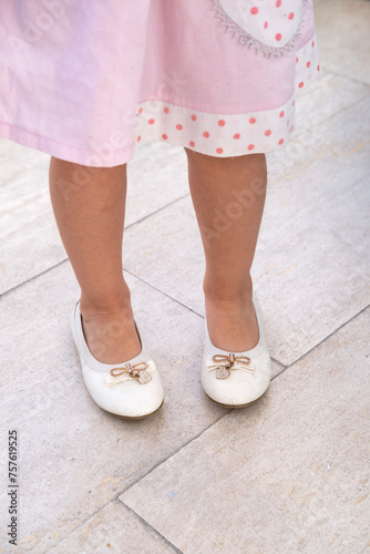 Little girl's legs in skirt, wearing white shoes with bows, charming innocence and playfulness of childhood, sense purity, youth and joyous moments being carefree