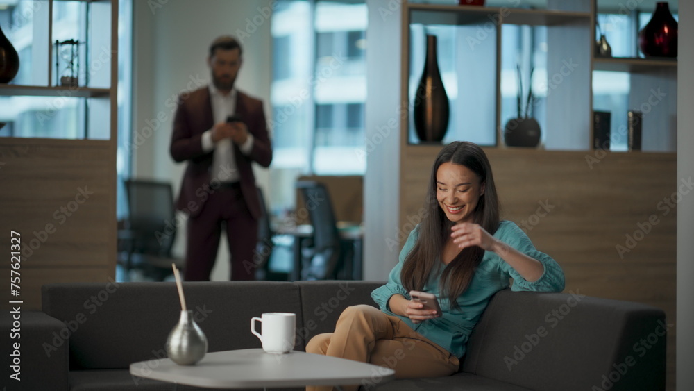 Happy businesswoman watching mobile phone at office lobby. Executive laughing