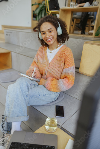 Woman sitting on floor, wearing headphones, using notebook