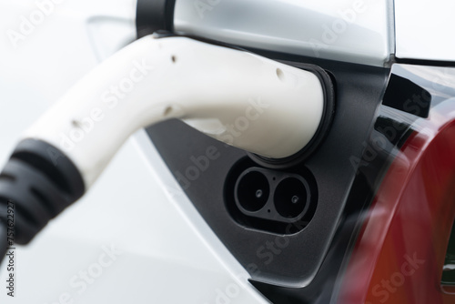 Closeup EV charger plug handle attached to electric vehicle port, recharging battery from charging station. Modern designed EV car and clean energy sustainability for better future concept. Synchronos