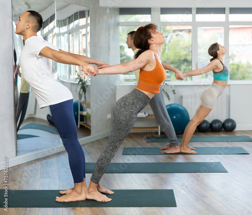 Male and female participant athletes practice pair yoga in studio during class. Lovers of active lifestyle perform doing standing deflection asana  backbend balance pose in gym