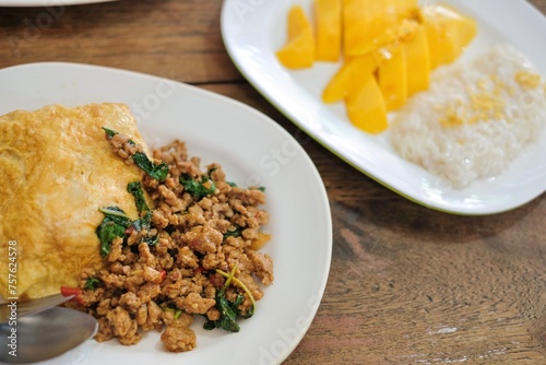 A plate of pad kra pao (holy basil pork mince stir-fry) with omelette and mixed grain rice, and a dessert of fresh mango with sticky rice at a street food stall in Phra Nakhon, Bangkok, Thailand
