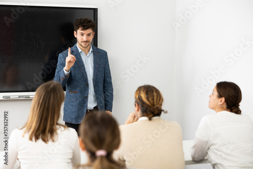 Positive male trainer  conducting advanced training courses to office employees sitting at desks in auditory