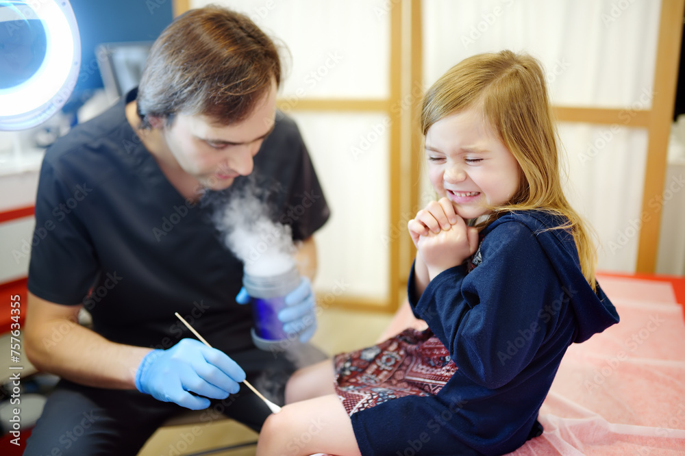 A caring doctor checks moles on the skin of a small child. Dermatologist remove of benign tumors with liquid nitrogen for cute preschooler girl. Baby fears of treat. - obrazy, fototapety, plakaty 