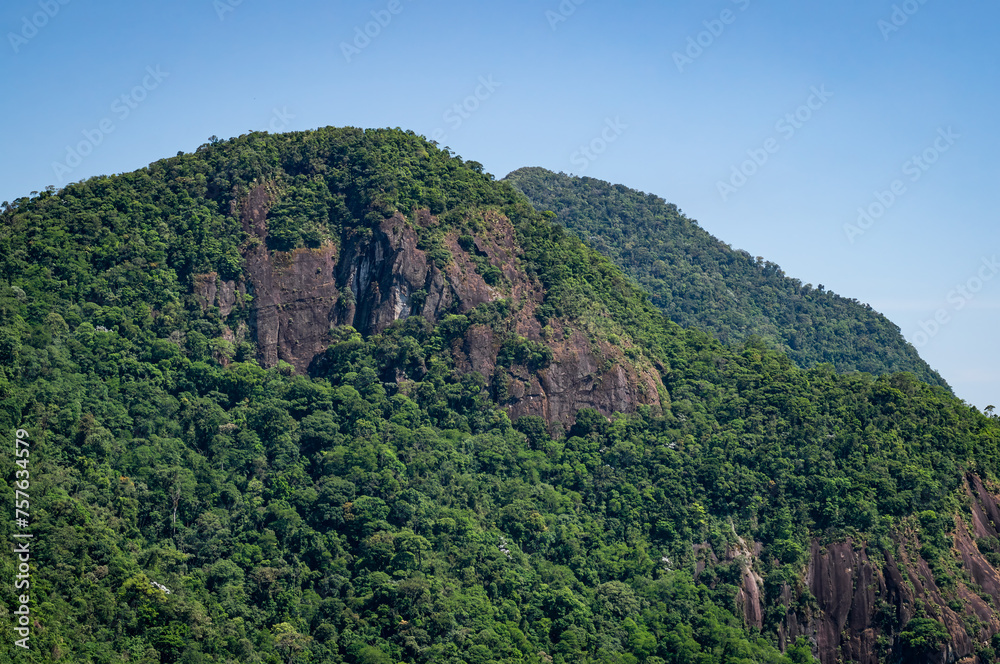 Fototapeta premium Rock formations covered by dense Atlantic Forest green vegetation viewed from Mirante do Cristo observation deck under summer afternoon sunny clear blue sky near Petropolis, Rio de Janeiro - Brazil.