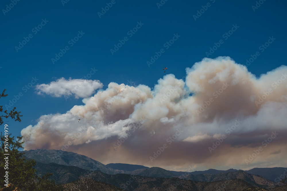 Panoramic view of fire fighting helicopters flying in a vast wildfire smoke rising into the blue sky over mountains in the countryside (climate change) (Curacaví, Chile)