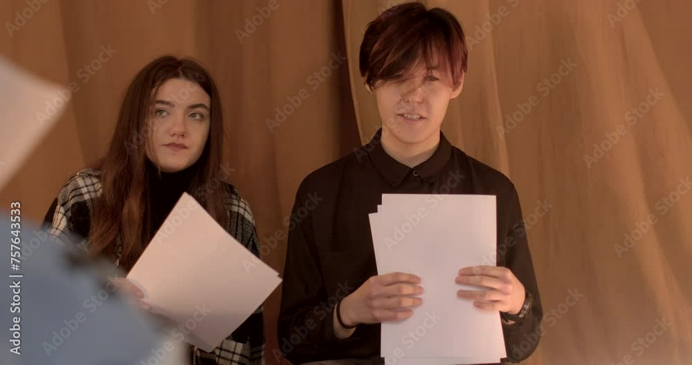 Portrait of a speaking Asian young man during theater mastery courses. Students hold scripts in hands, discussing literary readings. Group of young people talking, warm indoor. Portrait of a speaking Asian young man during theater mastery courses. Students hold scripts in hands, discussing literary readings. Group of young people talking, warm indoor.
