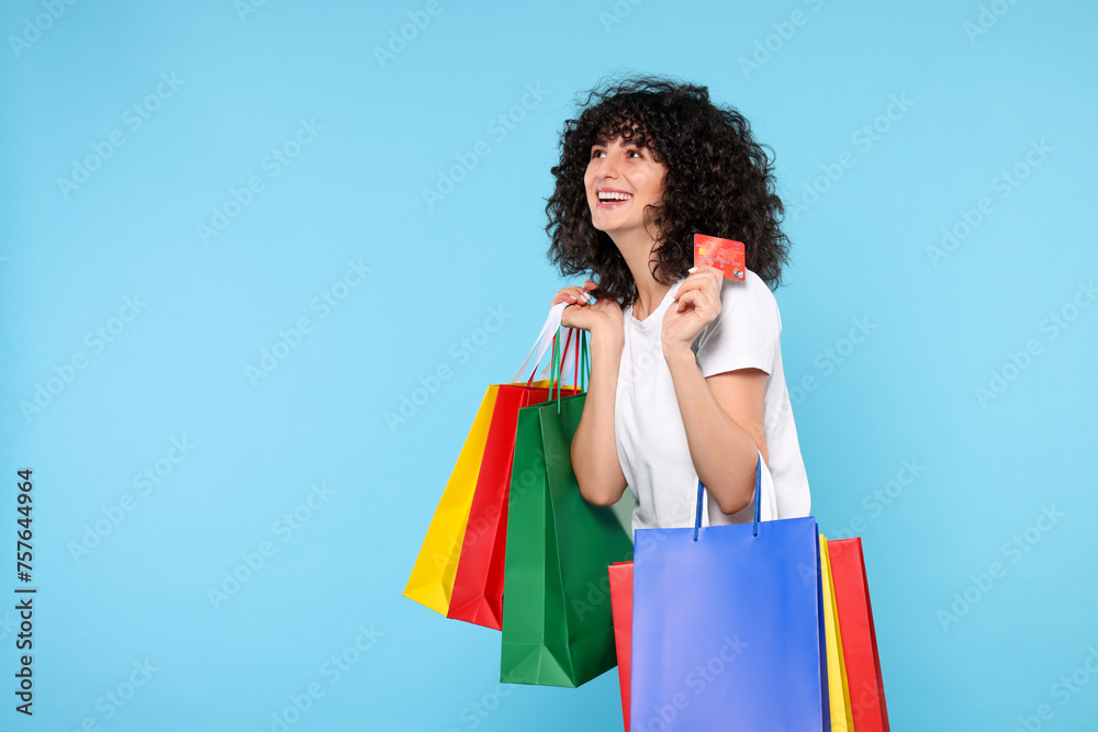 Happy young woman with shopping bags and credit cards on light blue background. Space for text Happy young woman with shopping bags and credit cards on light blue background. Space for text