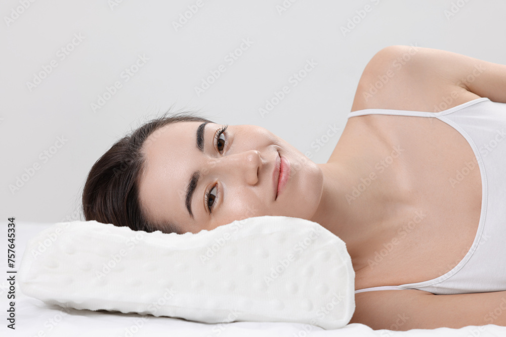 Obraz premium Woman lying on orthopedic pillow against light grey background