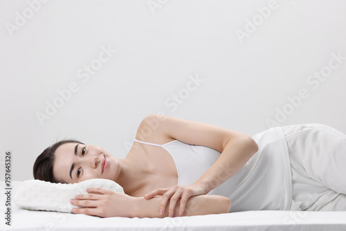 Woman lying on orthopedic pillow against light grey background, space for text