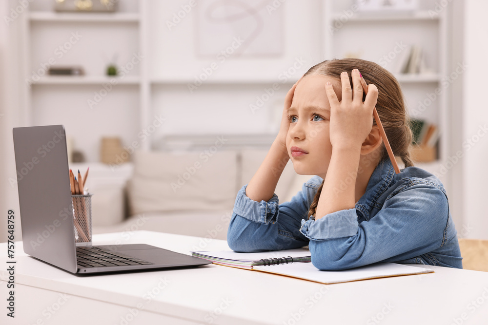 Little girl suffering from headache while doing homework at home