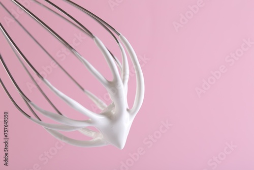 Whisk with whipped cream on pink background, closeup. Space for text