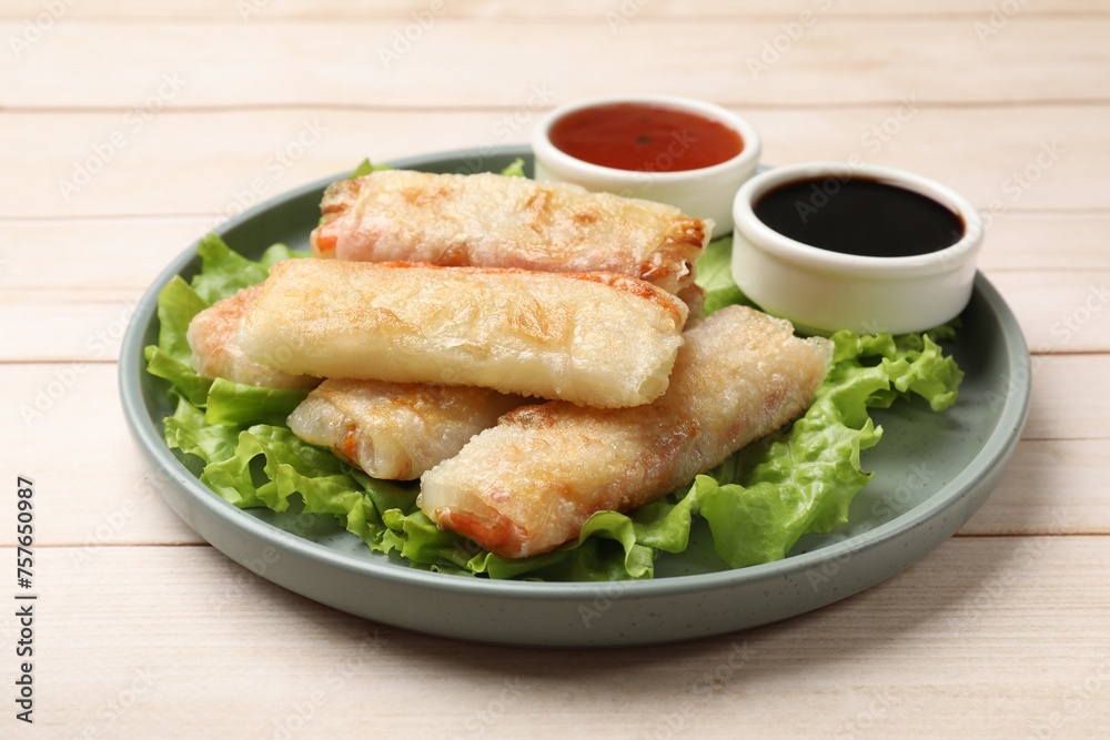 Delicious fried spring rolls and sauces on light wooden table