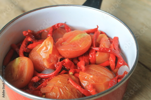 Chili, tomatoes and onions stewed in a red pot on the table photo